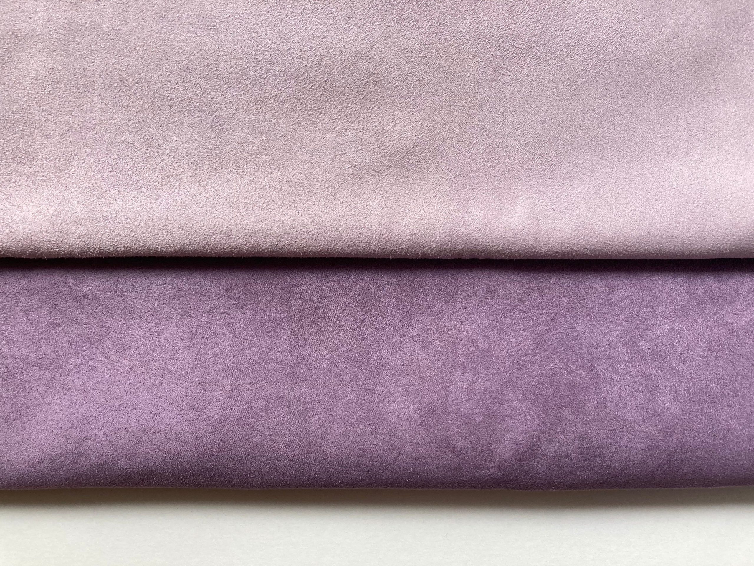 Two pieces of lilac faux suede fabric are shown stacked on top of each other against a white background (deux morceaux de tissu suédine synthétique sont empilés l’un sur l’autre sur un fond blanc, zwei Stücke Kunstwildlederstoff sind übereinander auf weißem Hintergrund gestapelt, dos piezas de tela de ante sintético están apiladas una sobre otra sobre un fondo blanco). The top piece is a pale, delicate lilac, and the bottom piece is a richer, deeper dark lilac (le morceau du dessus est un lilas pâle et délicat, et celui du dessous est un lilas foncé plus profond; das obere Stück ist ein blasses, zartes Flieder, das untere ist ein reiches, dunkleres Flieder; la pieza superior es un lila pálido y delicado, y la pieza inferior es un lila oscuro más intenso).