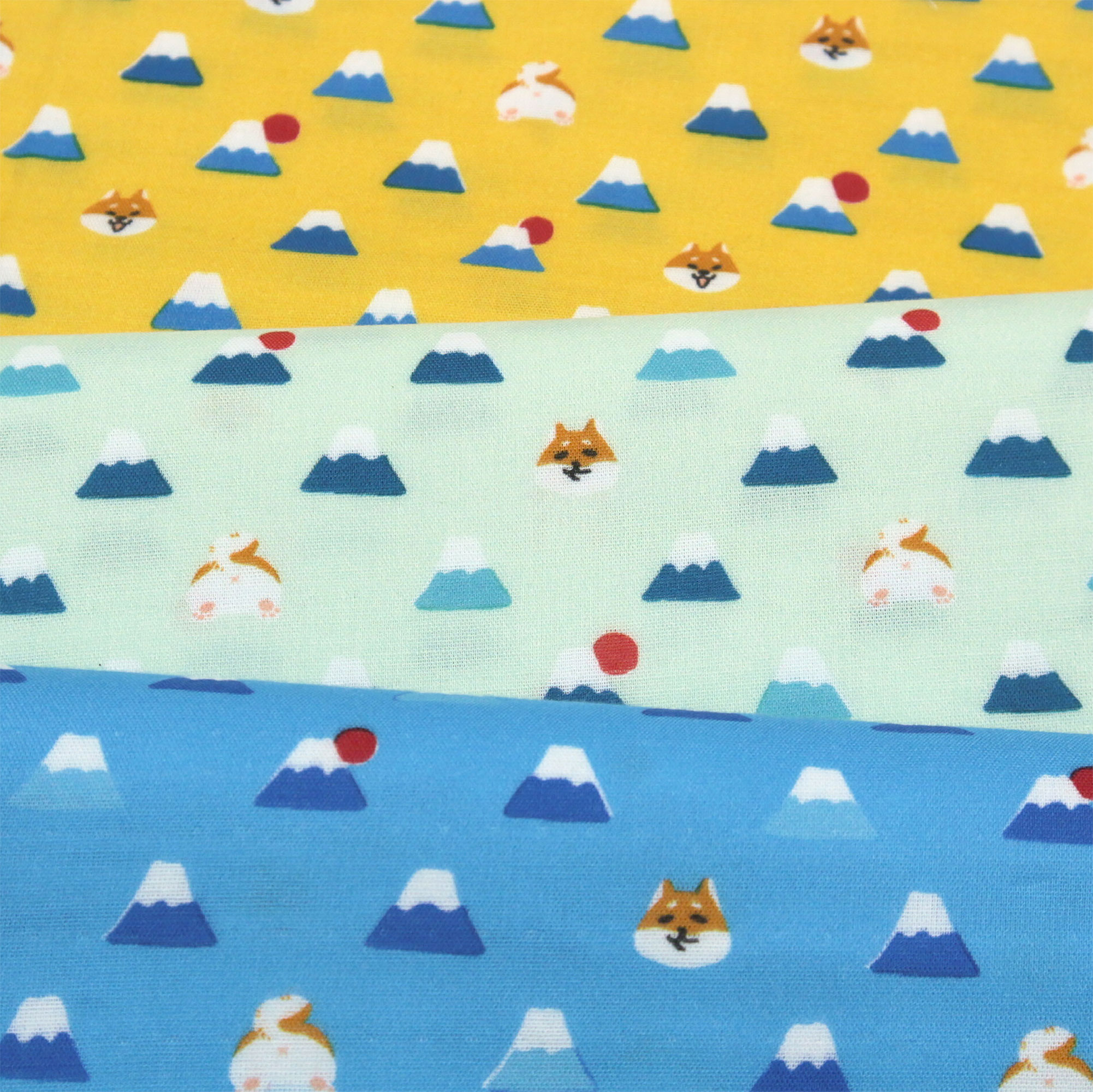 Mount Fuji and Shiba Inu Double Gauze: Three pieces of soft Japanese double gauze cotton fabric are shown stacked (trois morceaux de tissu double gaze de coton japonais doux sont empilés, drei Stück weicher japanischer Doppelgaze-Baumwollstoff sind gestapelt, se apilan tres piezas de tela de doble gasa de algodón japonés suave). The top piece has a mustard yellow background, the middle piece has a light green background, and the bottom piece has a light blue background (le morceau du dessus a un fond jaune moutarde, celui du milieu un fond vert clair, et celui du dessous un fond bleu clair; das obere Stück hat einen senfgelben Hintergrund, das mittlere einen hellgrünen Hintergrund, und das untere einen hellblauen Hintergrund; la pieza superior tiene un fondo amarillo mostaza, la del medio un fondo verde claro, y la inferior un fondo azul claro). All fabrics feature a repeating pattern of stylized Mount Fuji with snowy caps and a red sun behind it, along with various cute Shiba Inu dog faces (tous les tissus présentent un motif répété du Mont Fuji stylisé avec des sommets enneigés et un soleil rouge derrière, ainsi que diverses têtes mignonnes de chiens Shiba Inu; alle Stoffe zeigen ein sich wiederholendes Muster des stilisierten Berges Fuji mit schneebedecktem Gipfel und einer roten Sonne dahinter, zusammen mit verschiedenen niedlichen Shiba Inu Hundegesichtern; todas las telas presentan un patrón repetido del Monte Fuji estilizado con cumbres nevadas y un sol rojo detrás, junto con varias caritas adorables de perros Shiba Inu).